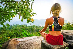 Woman wearing Chakra Sports Bra top sitting on a rock in yoga pose.